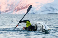 Gary rolling his kayak against pink-lit mountains