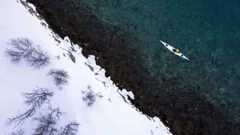 Aerial view of Gary kayaking beside the snowy Arctic shore